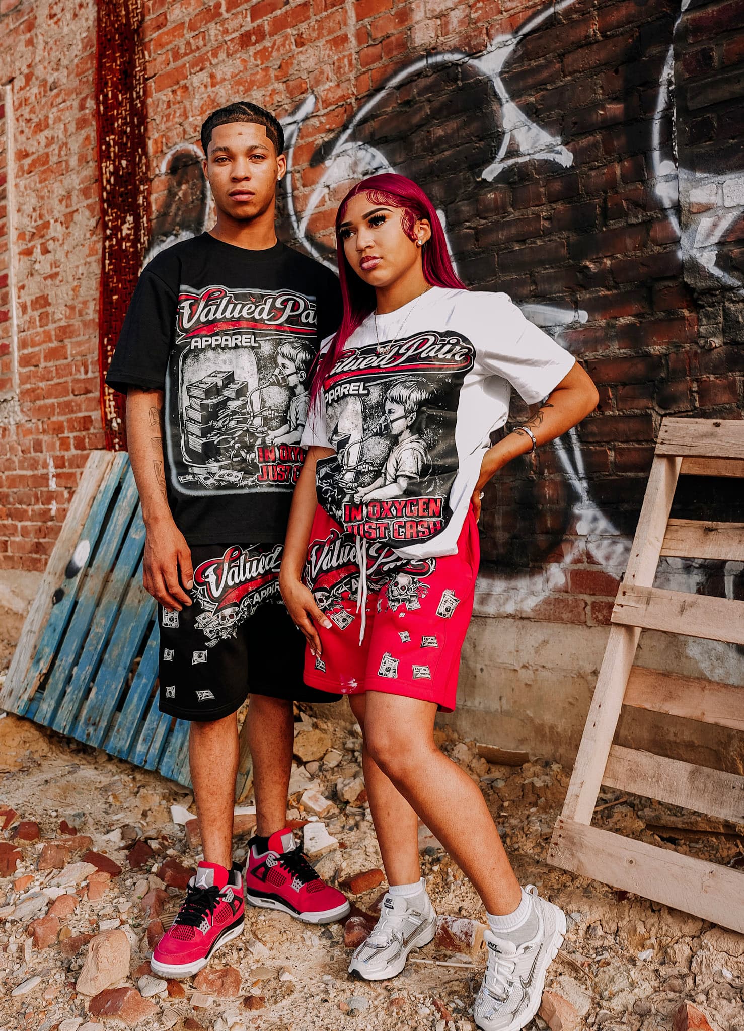 Drop 01 — both Oxygen sets worn against a graffiti brick wall